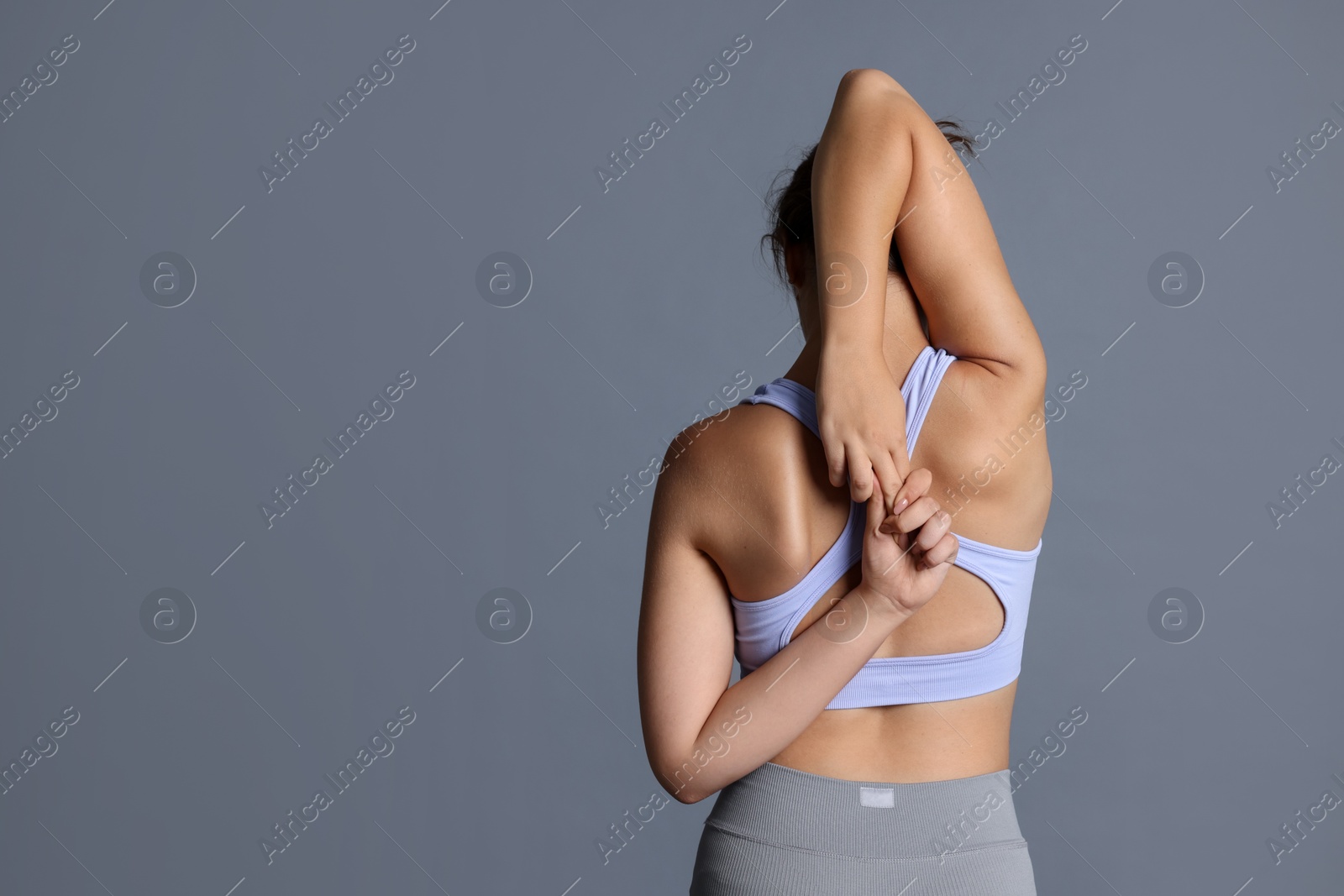 Teenage girl in sportswear stretching on grey background, back view. Space for text Photo of Teenage girl in sportswear stretching on grey background, back view. Space for text