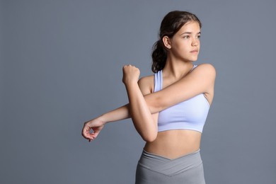 Photo of Teenage girl in sportswear stretching on grey background, space for text