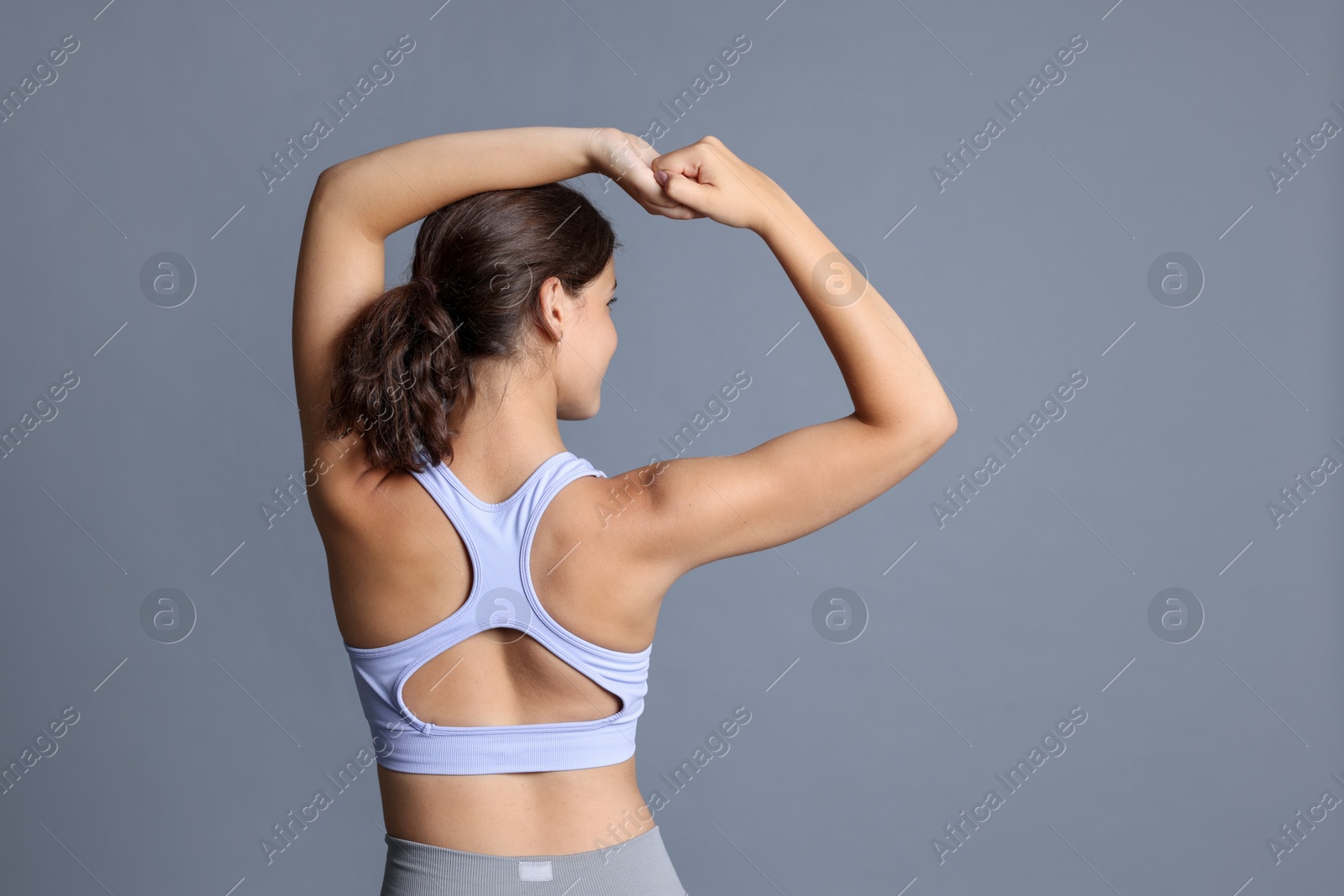 Teenage girl in sportswear stretching on grey background, back view. Space for text Photo of Teenage girl in sportswear stretching on grey background, back view. Space for text