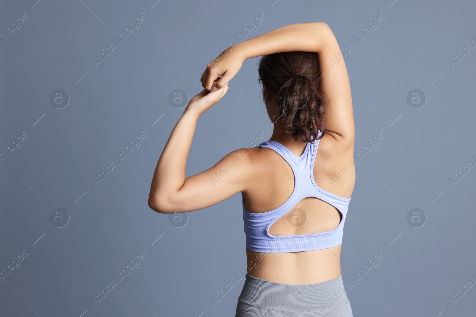 Teenage girl in sportswear stretching on grey background, back view. Space for text Photo of Teenage girl in sportswear stretching on grey background, back view. Space for text