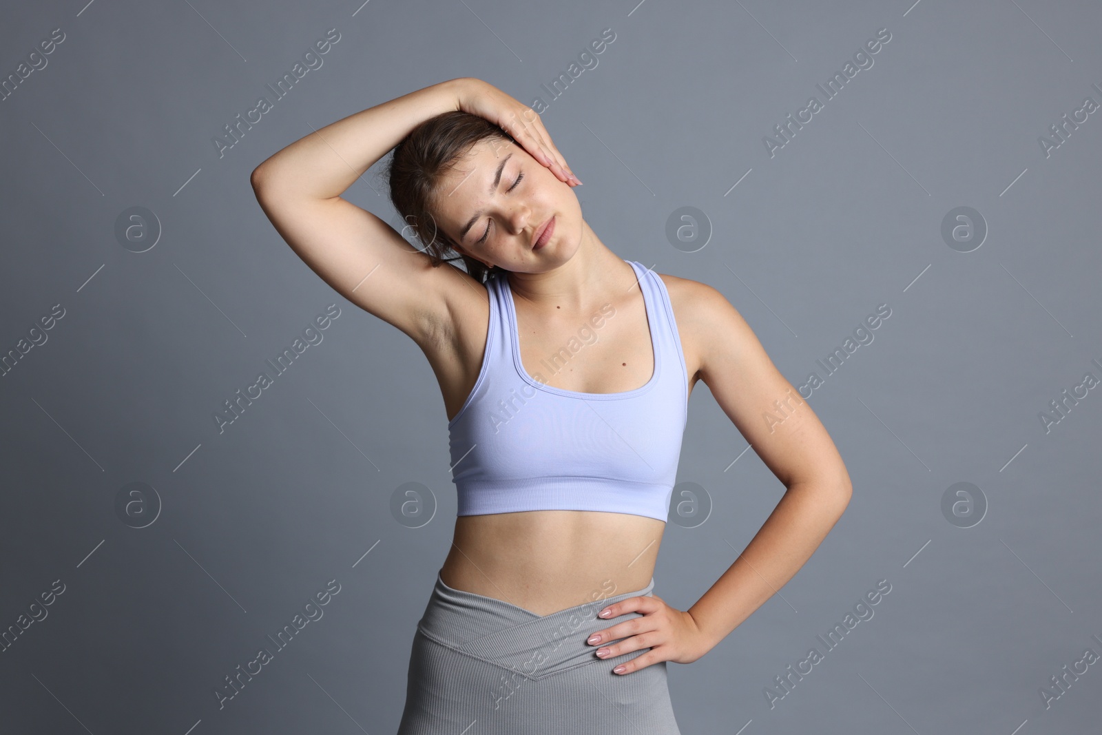 Teenage girl in sportswear stretching on grey background Photo of Teenage girl in sportswear stretching on grey background
