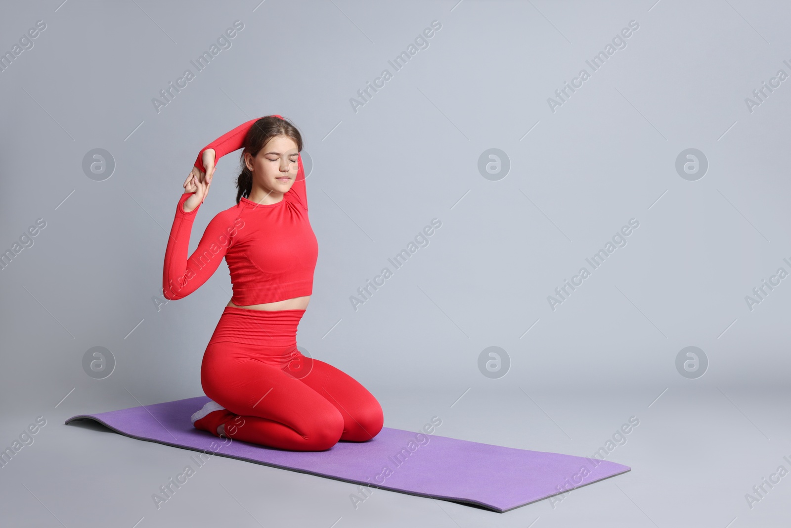 Teenage girl in sportswear stretching on mat against grey background, space for text Photo of Teenage girl in sportswear stretching on mat against grey background, space for text