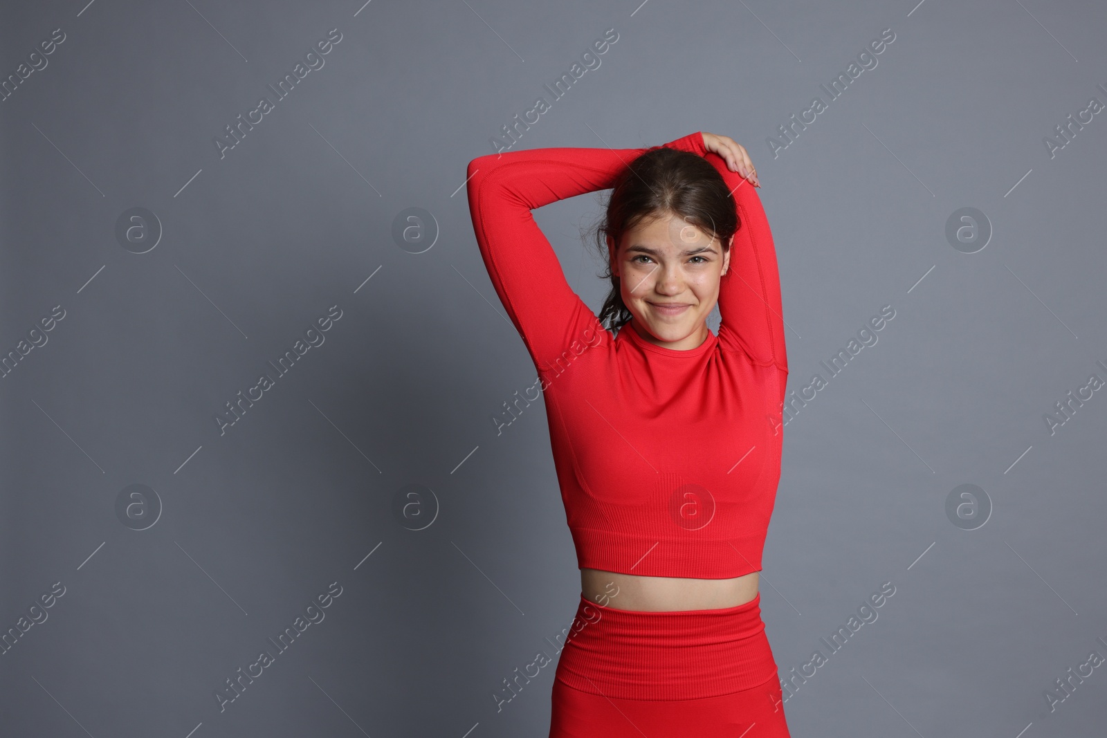 Teenage girl in sportswear stretching on grey background, space for text Photo of Teenage girl in sportswear stretching on grey background, space for text