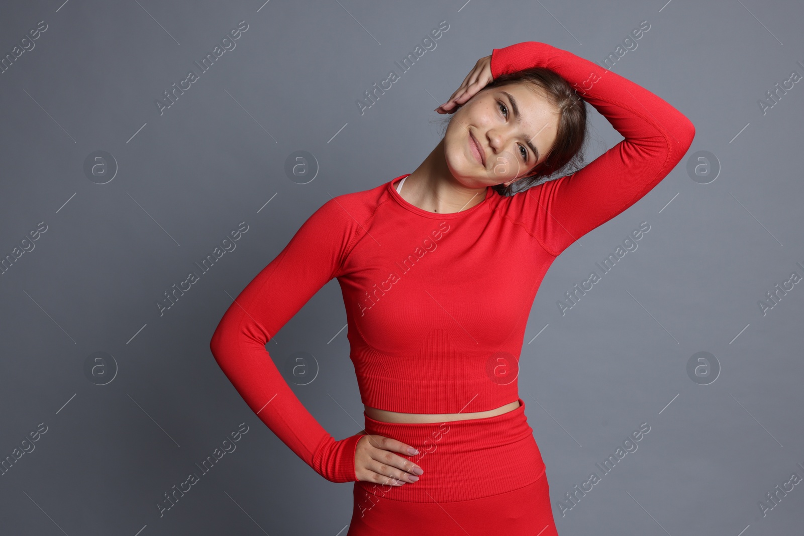 Teenage girl in sportswear stretching on grey background Photo of Teenage girl in sportswear stretching on grey background