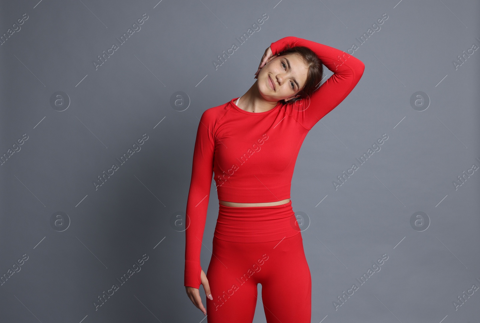 Teenage girl in sportswear stretching on grey background Photo of Teenage girl in sportswear stretching on grey background
