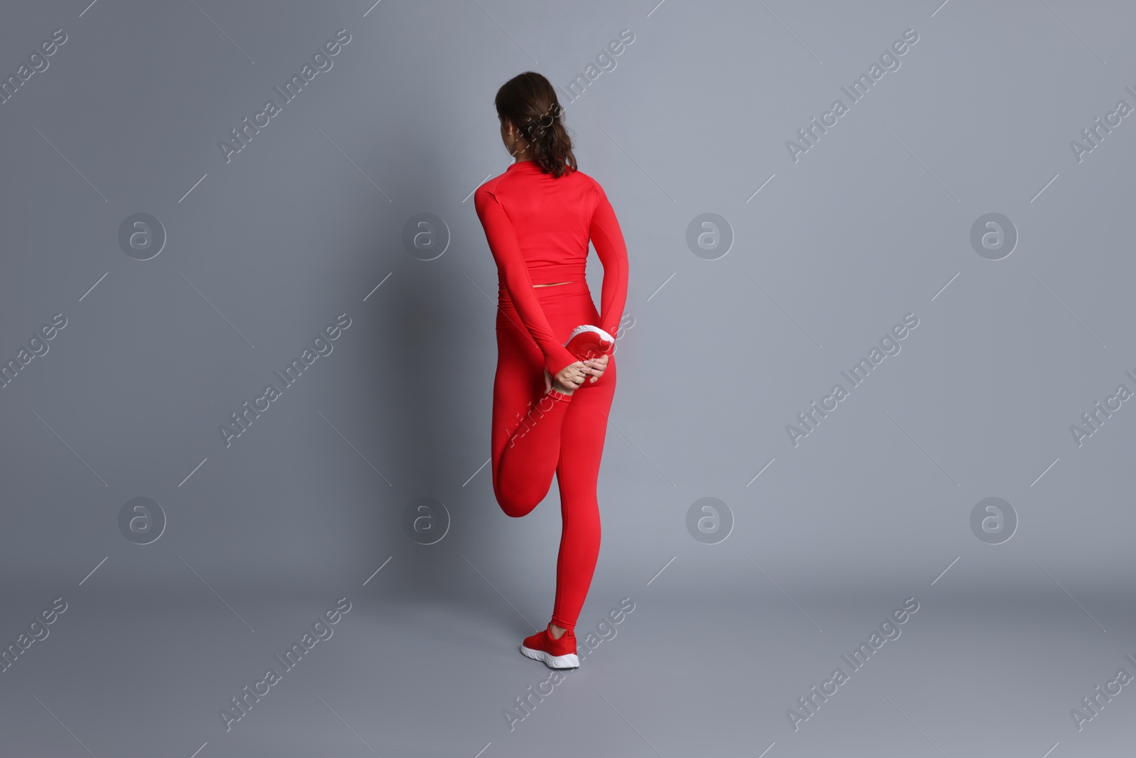 Teenage girl in sportswear stretching on grey background, back view Photo of Teenage girl in sportswear stretching on grey background, back view
