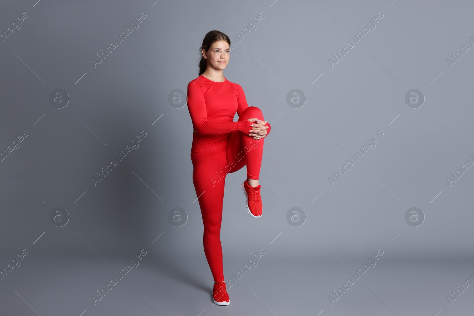 Teenage girl in sportswear stretching on grey background Photo of Teenage girl in sportswear stretching on grey background