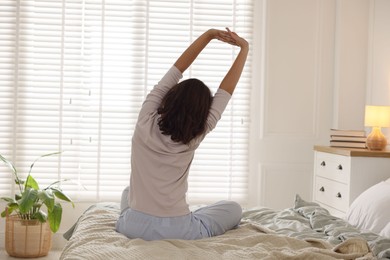 Photo of Teenage girl stretching on bed at home, back view