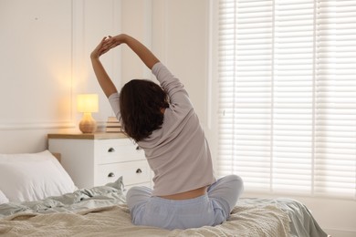 Photo of Teenage girl stretching on bed at home, back view