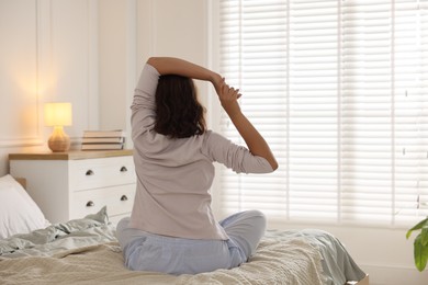 Photo of Teenage girl stretching on bed at home, back view