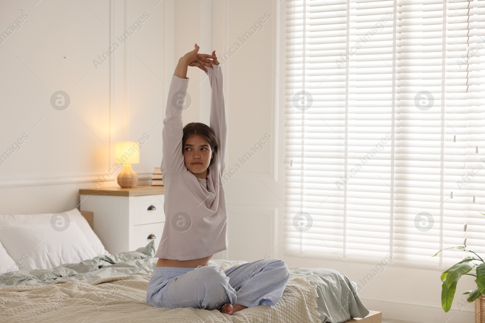Teenage girl stretching on bed at home, space for text Photo of Teenage girl stretching on bed at home, space for text