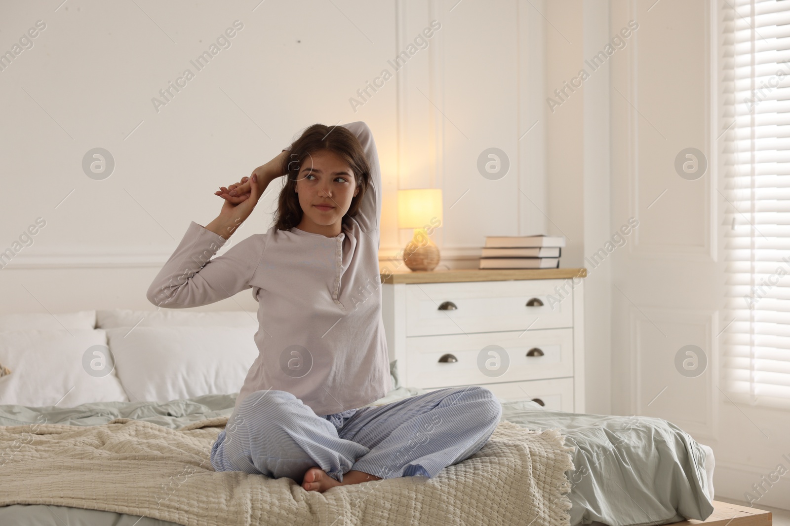 Teenage girl stretching on bed at home, space for text Photo of Teenage girl stretching on bed at home, space for text