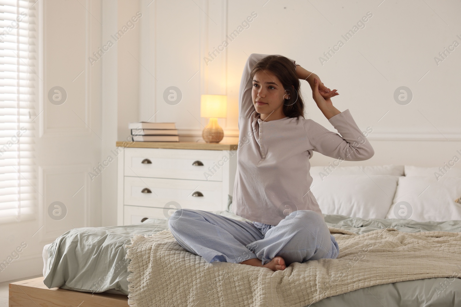 Teenage girl stretching on bed at home, space for text Photo of Teenage girl stretching on bed at home, space for text