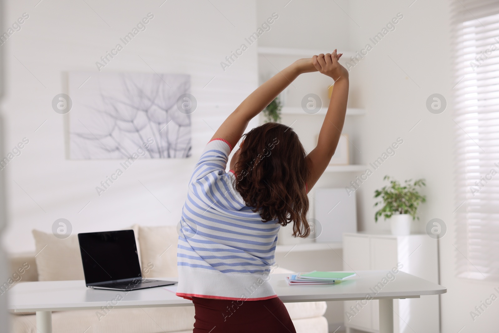 Photo of Teenage girl stretching at table indoors, back view