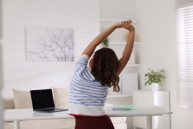 Photo of Teenage girl stretching at table indoors, back view