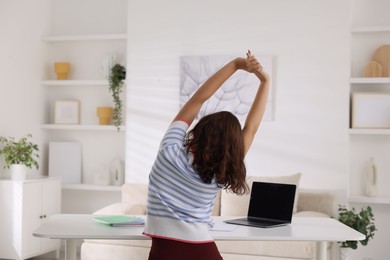 Photo of Teenage girl stretching at table indoors, back view