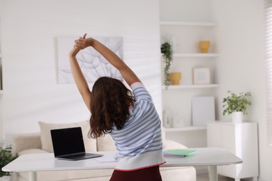Photo of Teenage girl stretching at table indoors, back view