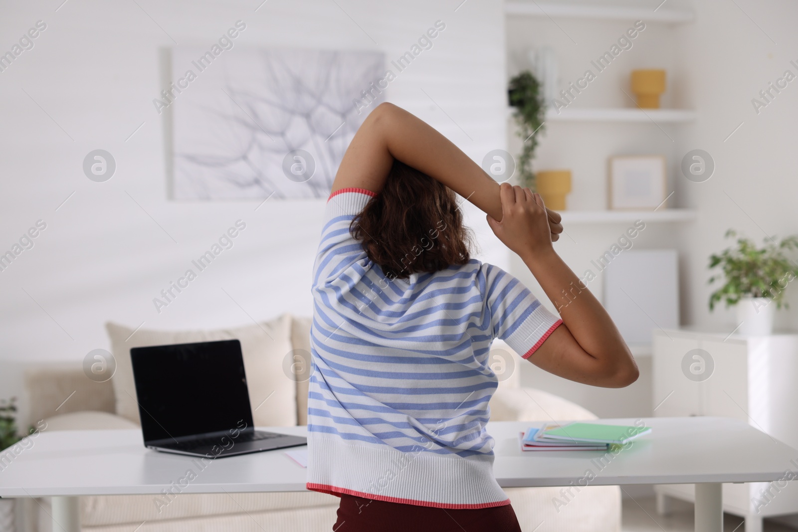 Photo of Teenage girl stretching at table indoors, back view