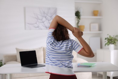 Photo of Teenage girl stretching at table indoors, back view