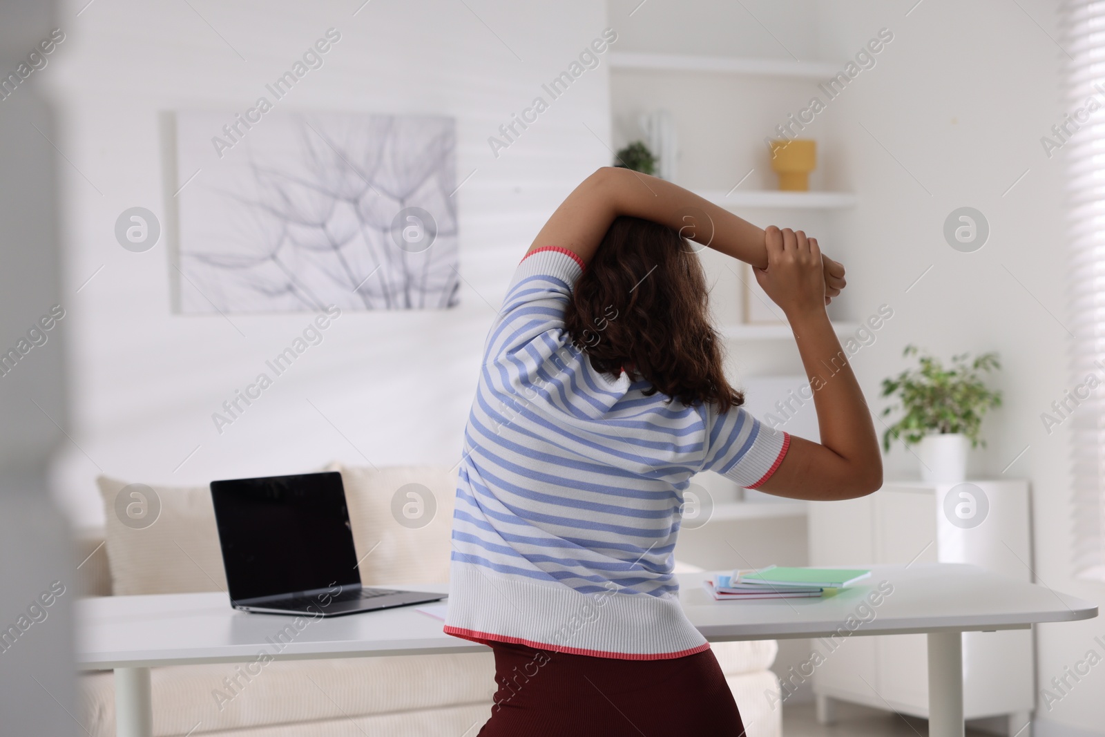 Photo of Teenage girl stretching at table indoors, back view