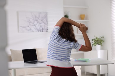 Photo of Teenage girl stretching at table indoors, back view