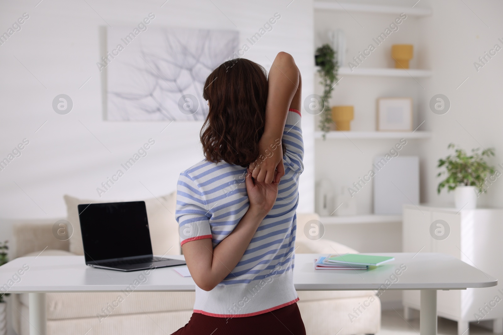 Photo of Teenage girl stretching at table indoors, back view
