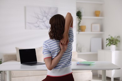 Photo of Teenage girl stretching at table indoors, back view