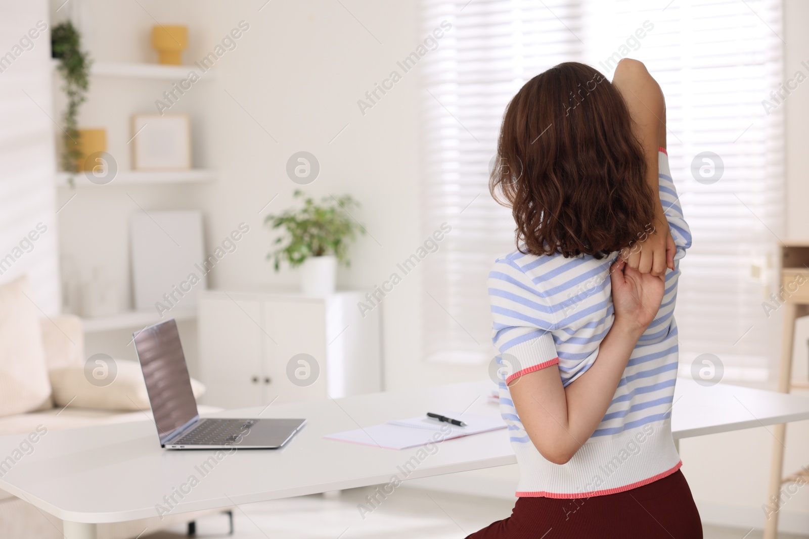 Photo of Teenage girl stretching at table indoors, back view