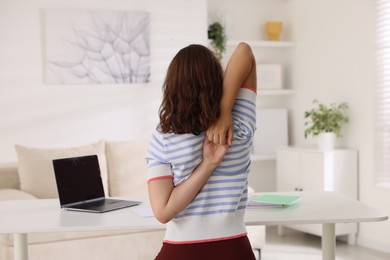 Photo of Teenage girl stretching at table indoors, back view