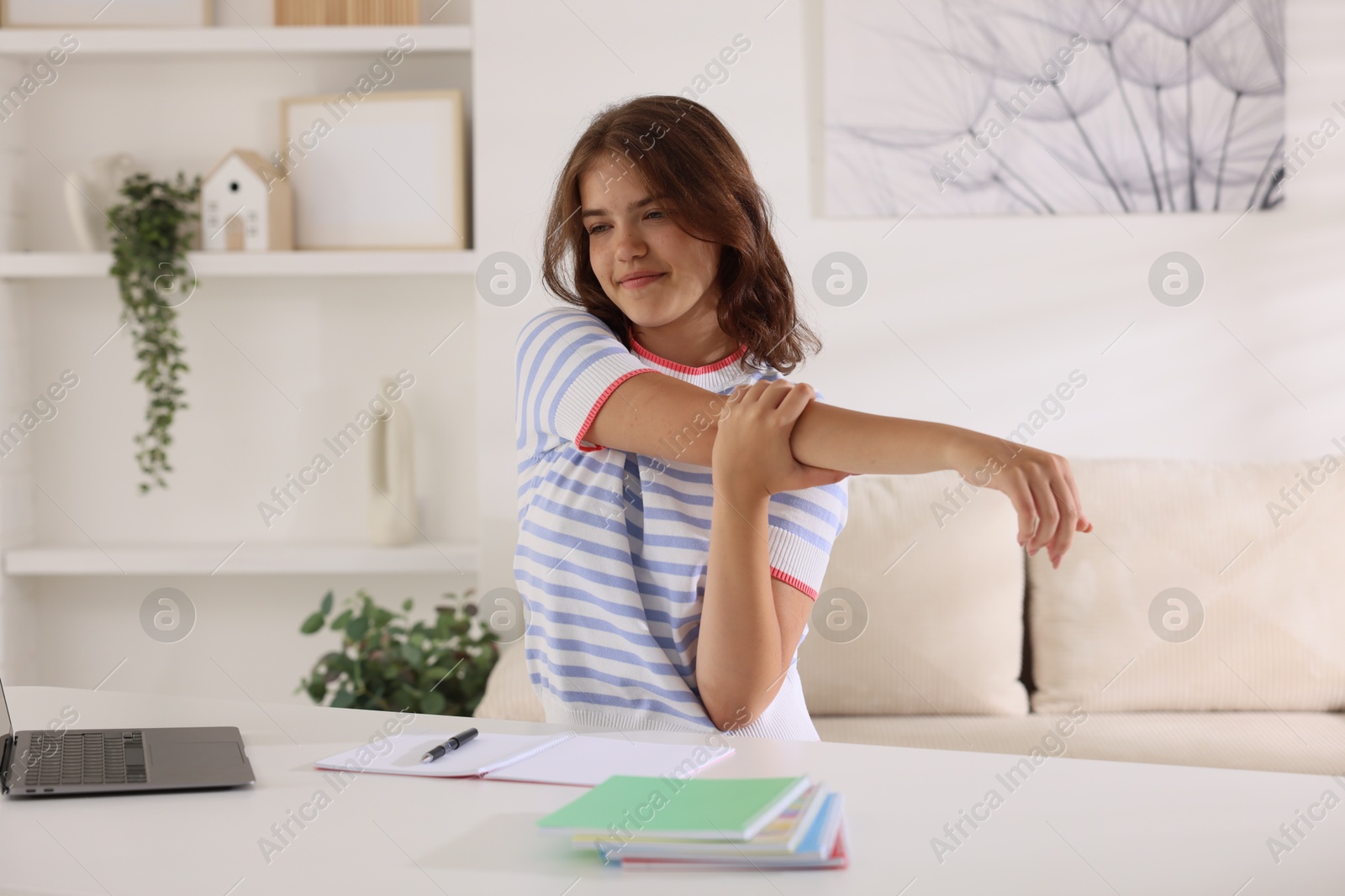 Beautiful teenage girl stretching at table indoors Photo of Beautiful teenage girl stretching at table indoors