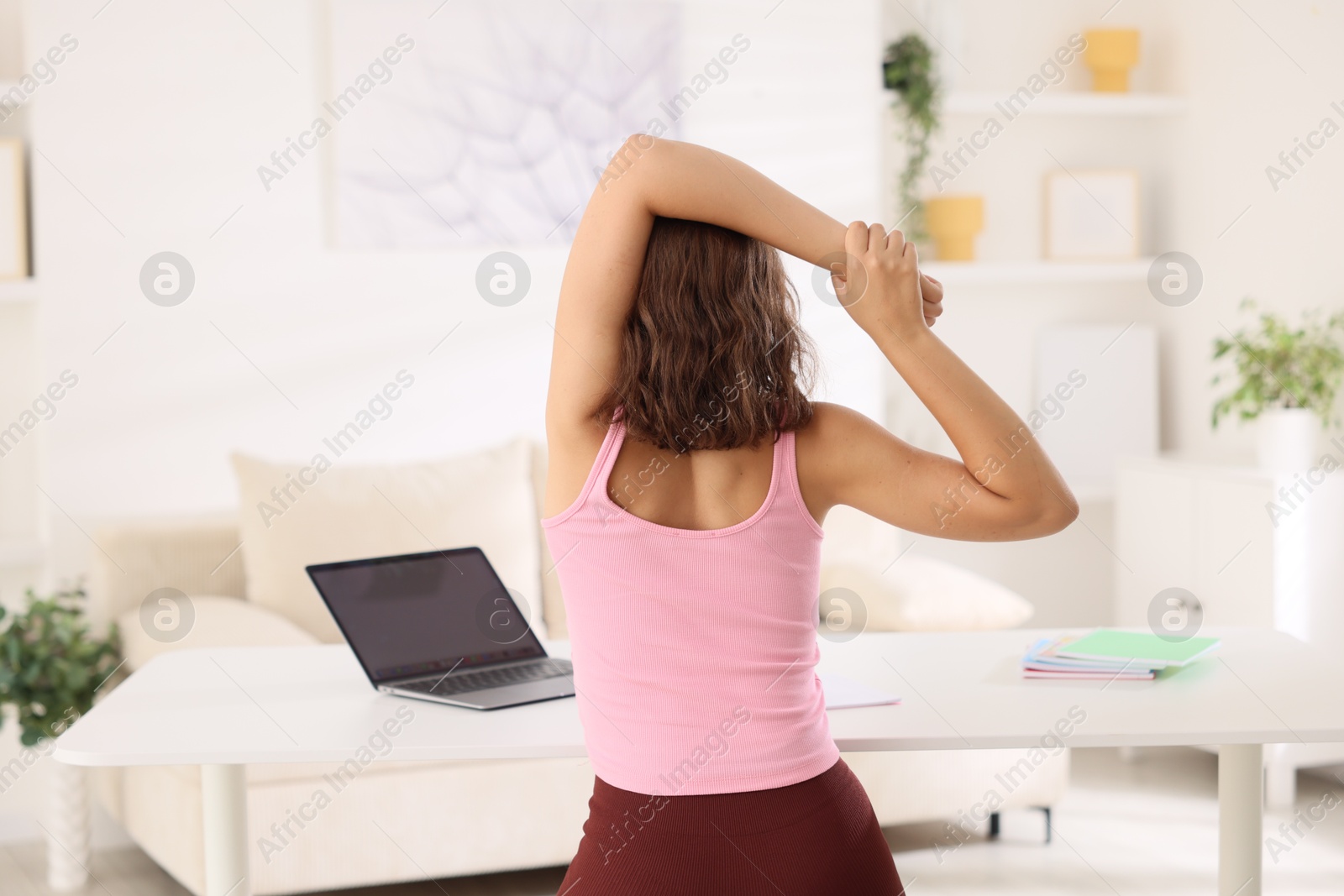 Photo of Teenage girl stretching at table indoors, back view