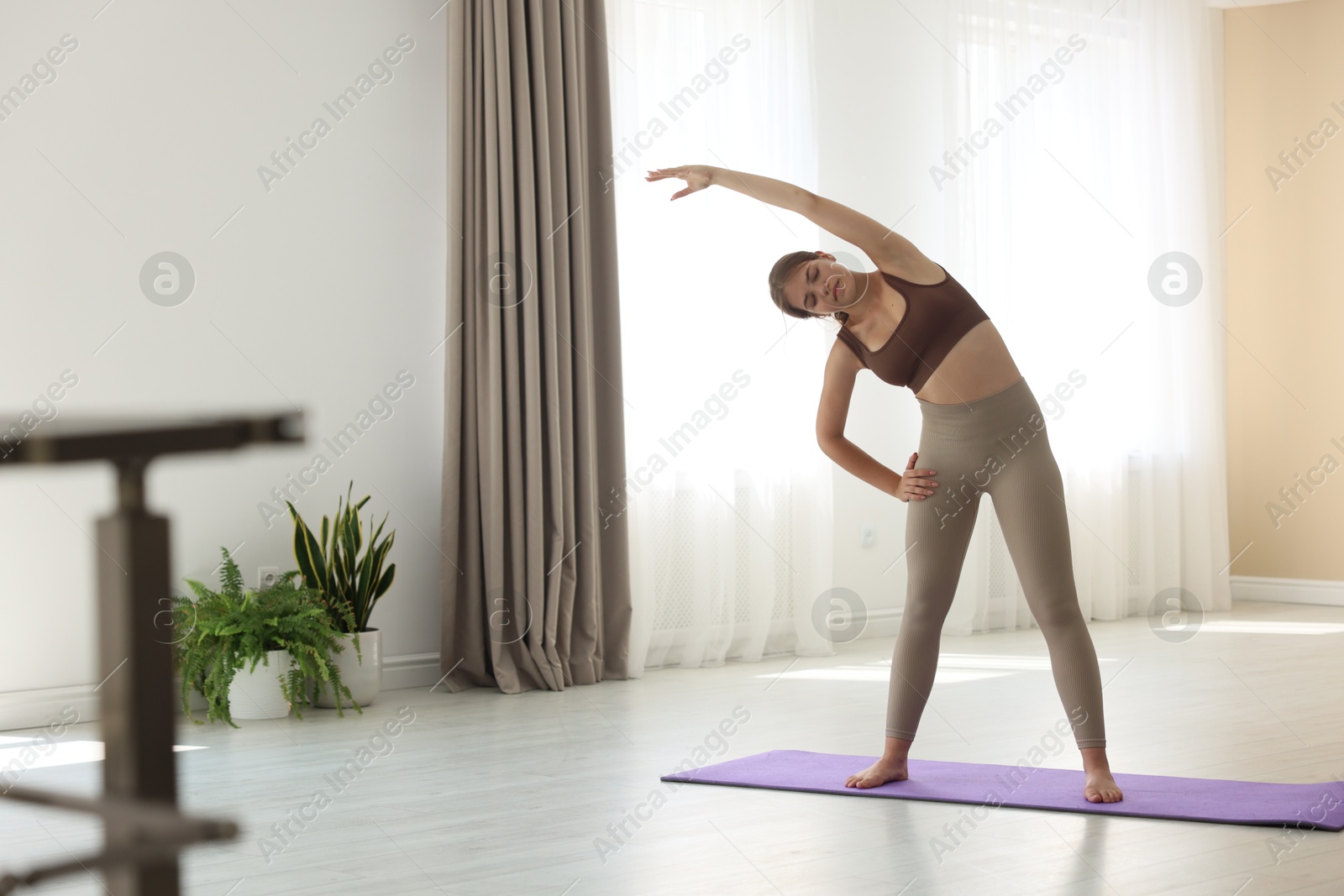 Photo of Teenage girl in sportswear stretching on mat indoors, space for text