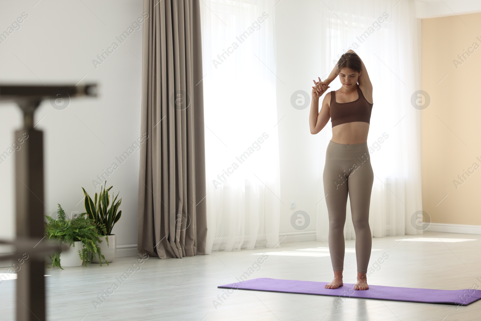 Photo of Teenage girl in sportswear stretching on mat indoors, space for text