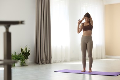Photo of Teenage girl in sportswear stretching on mat indoors, space for text