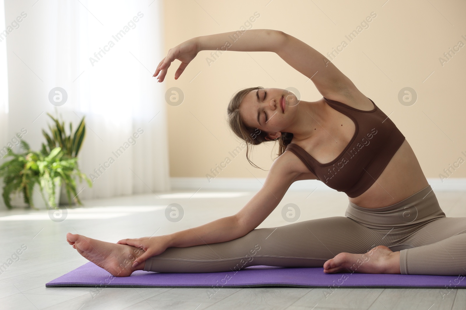 Photo of Teenage girl in sportswear stretching on mat indoors