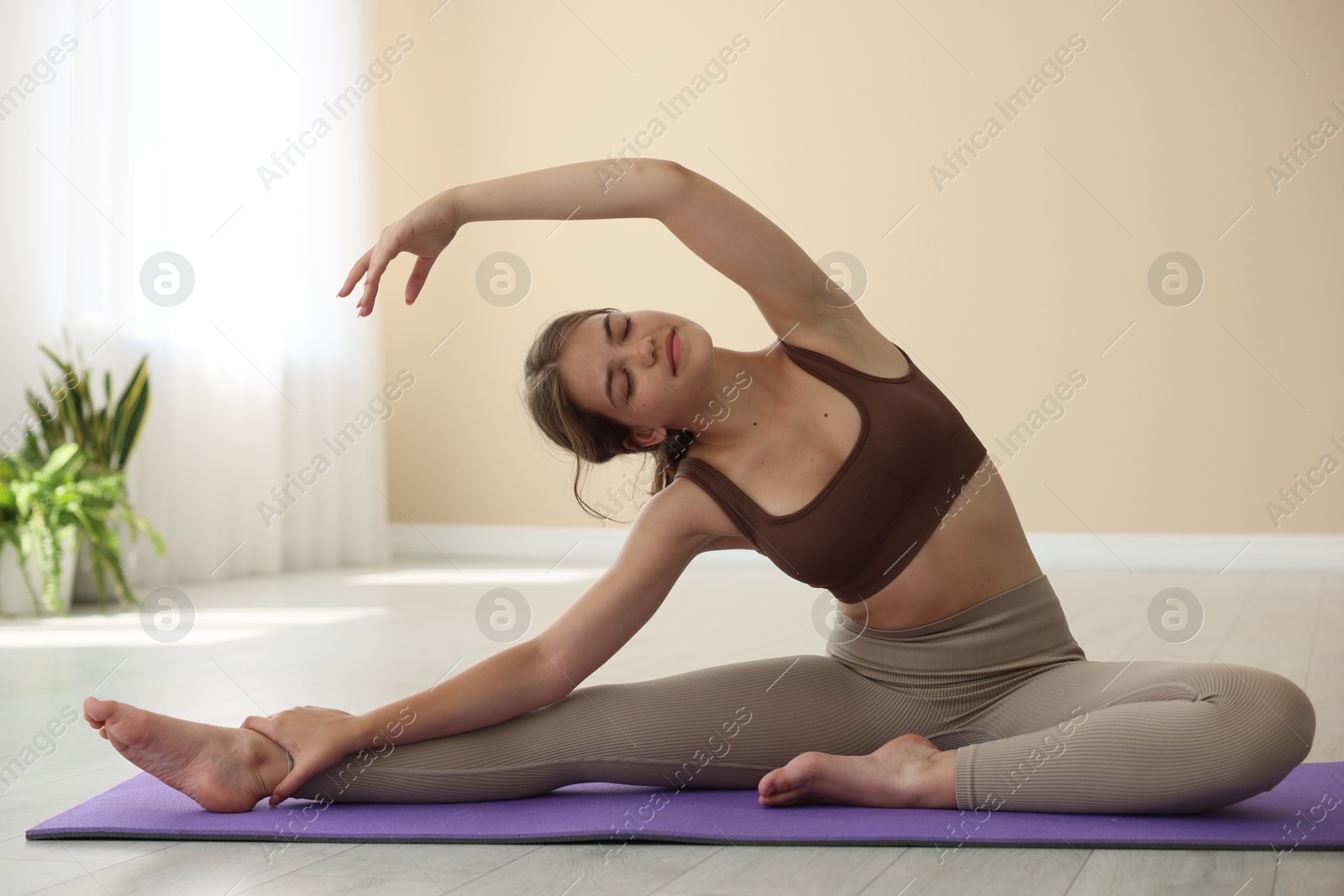 Photo of Teenage girl in sportswear stretching on mat indoors