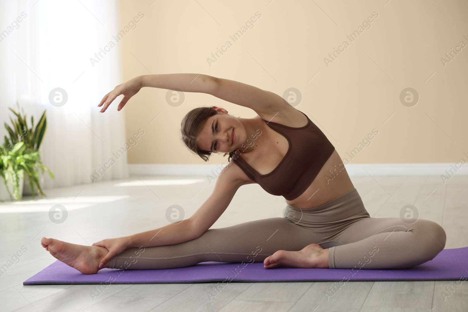 Photo of Teenage girl in sportswear stretching on mat indoors