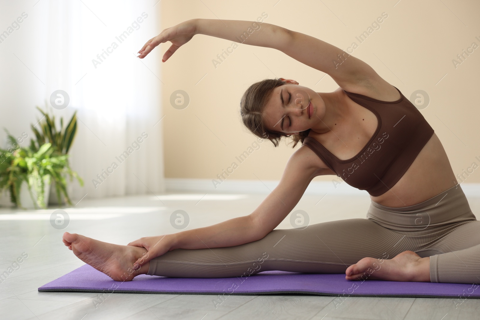 Photo of Teenage girl in sportswear stretching on mat indoors