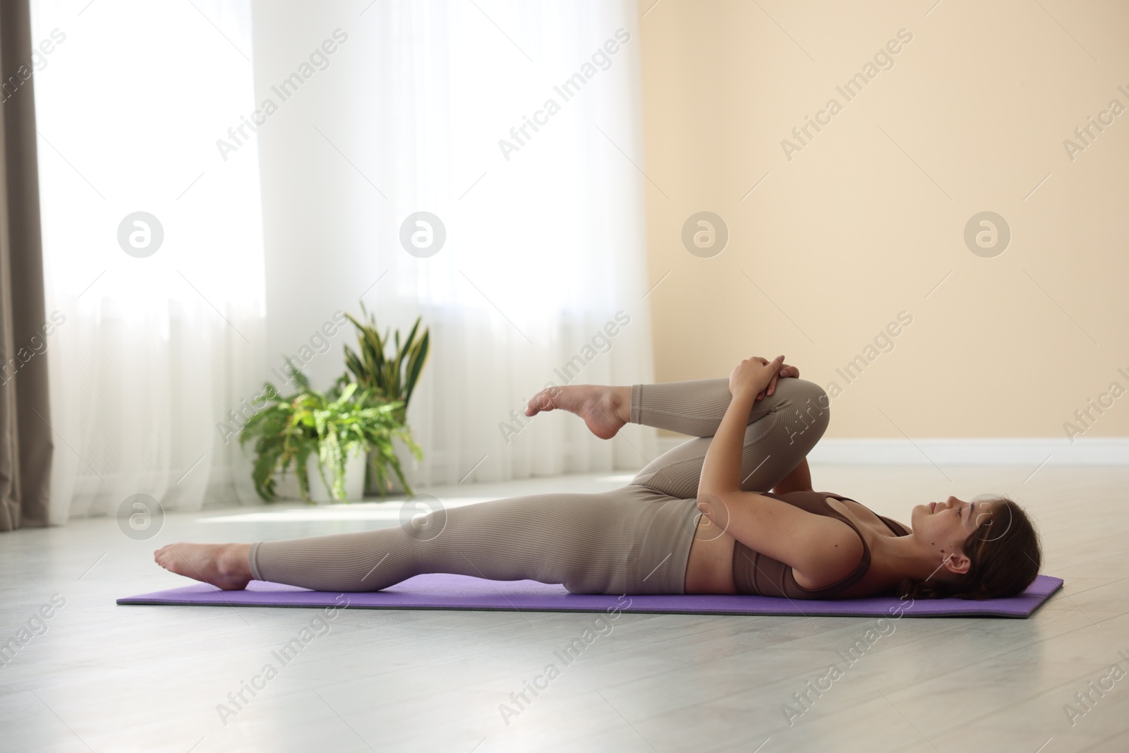 Photo of Teenage girl in sportswear stretching on mat indoors