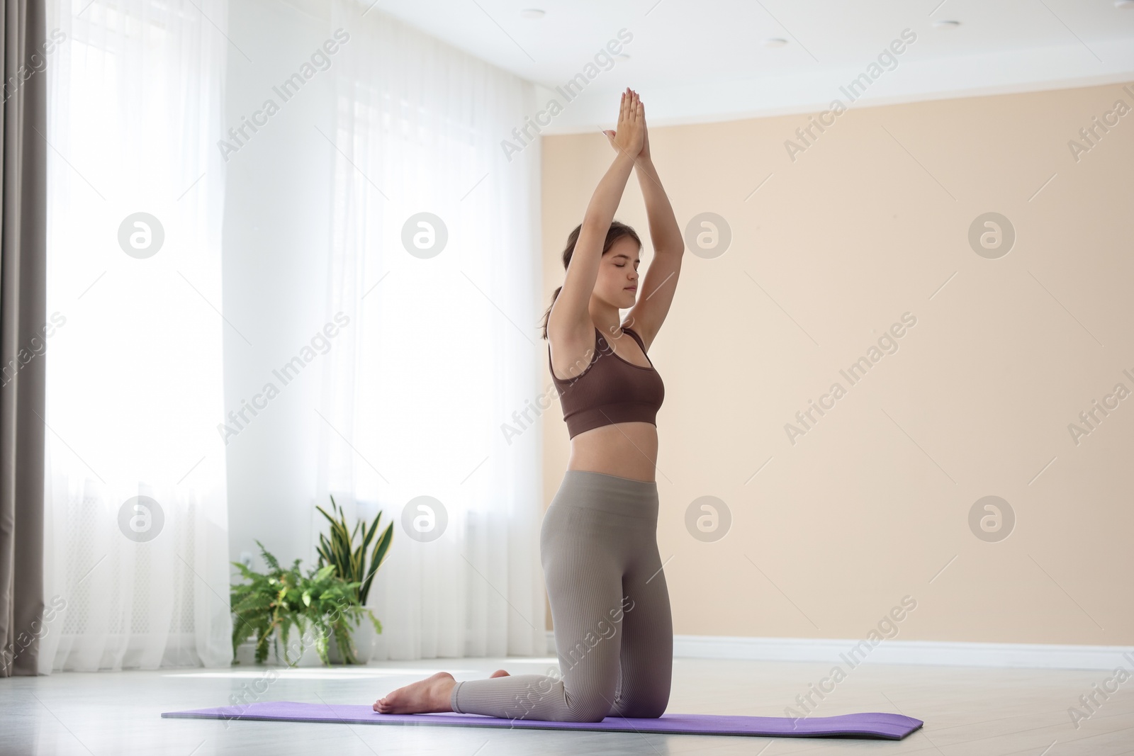 Photo of Teenage girl in sportswear stretching on mat indoors