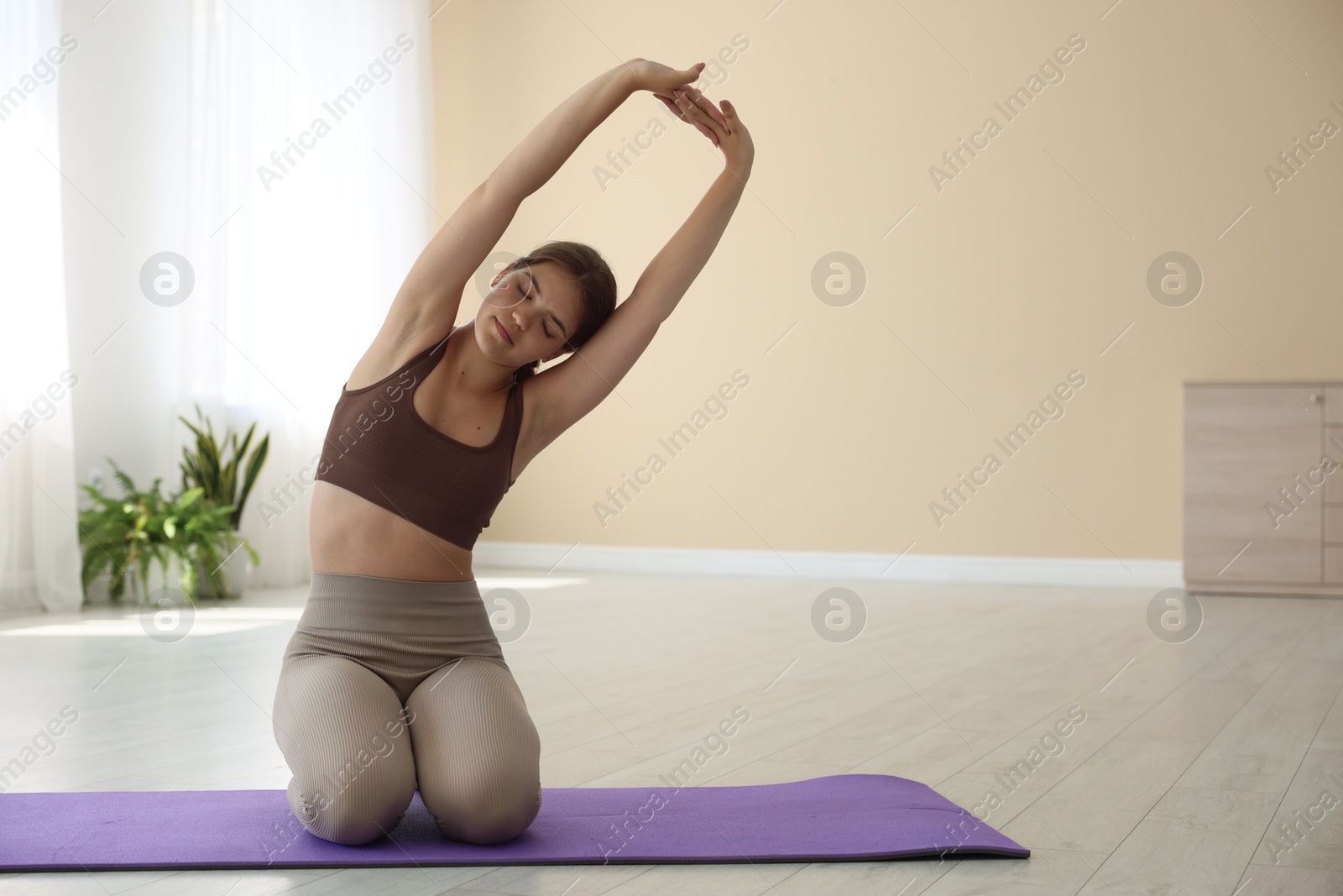 Photo of Teenage girl in sportswear stretching on mat indoors, space for text