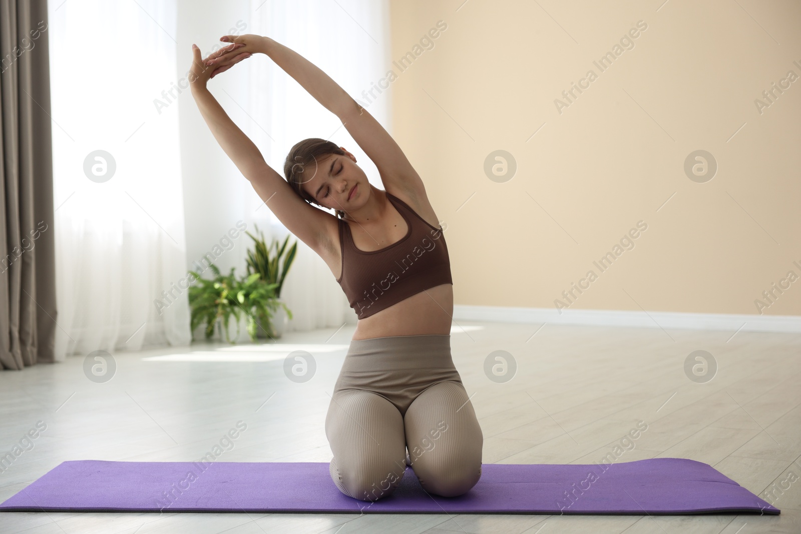 Photo of Teenage girl in sportswear stretching on mat indoors