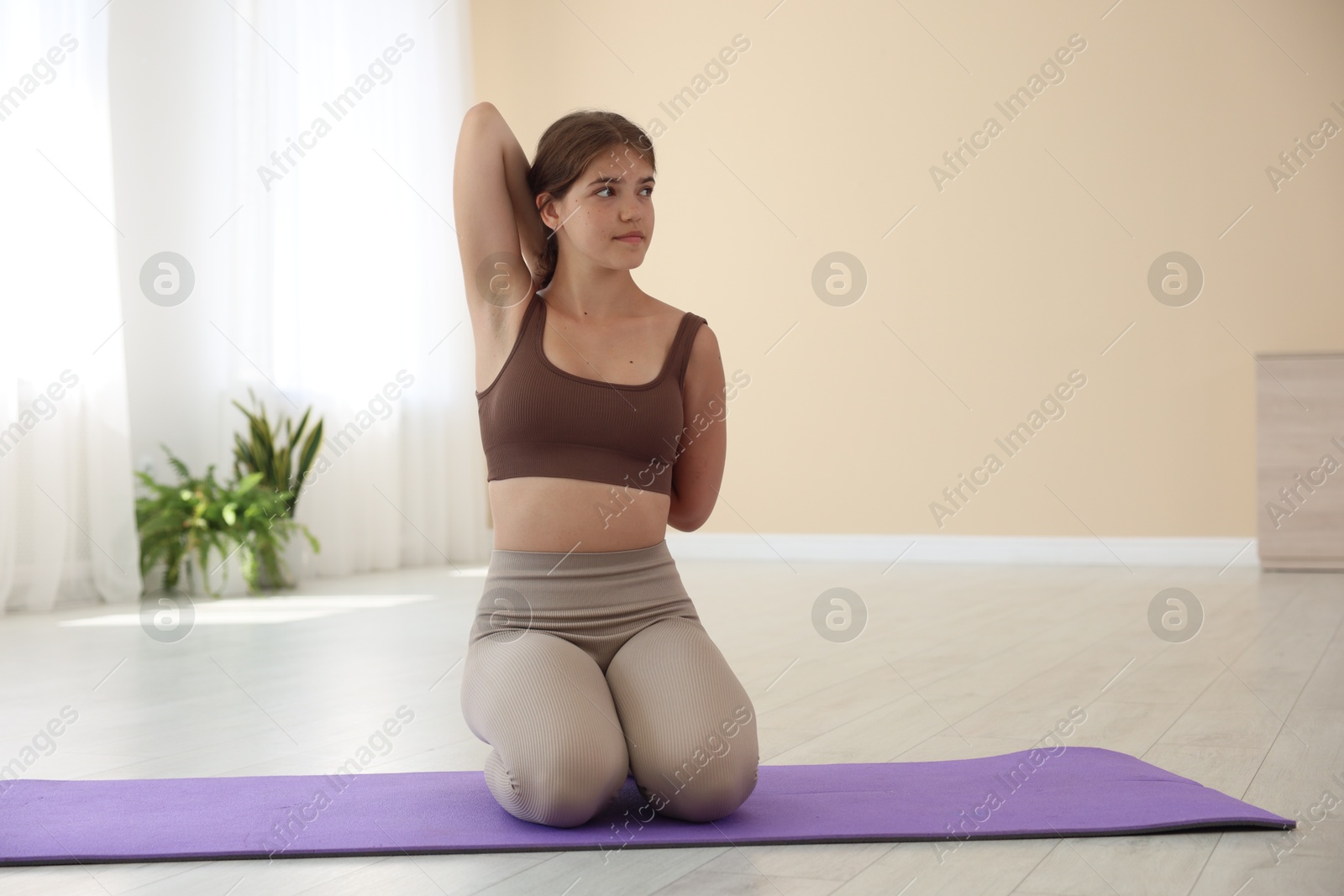 Photo of Teenage girl in sportswear stretching on mat indoors