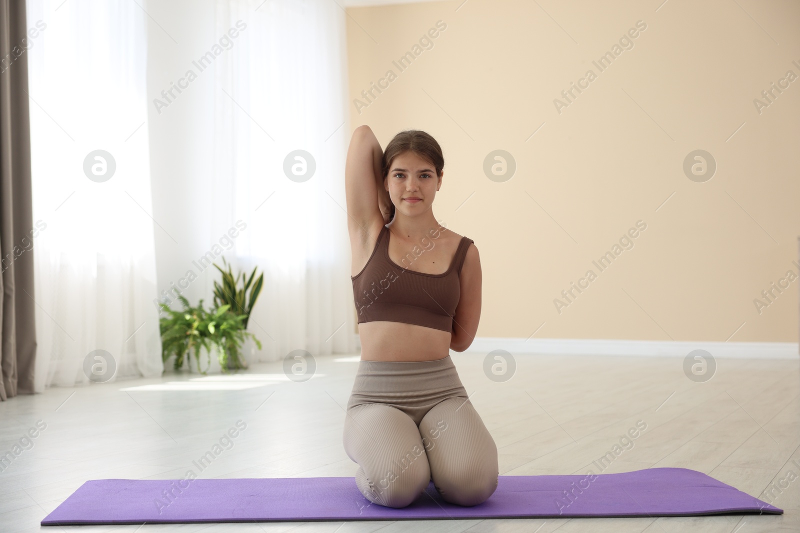 Photo of Teenage girl in sportswear stretching on mat indoors