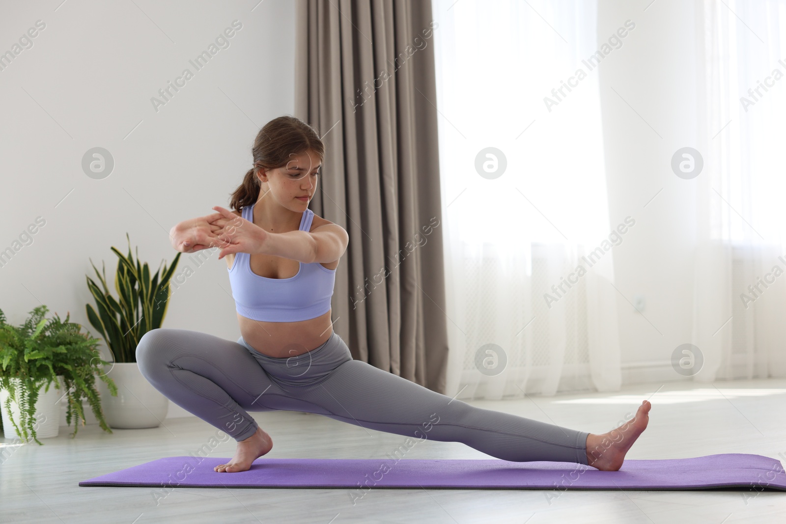 Photo of Teenage girl in sportswear stretching on mat indoors
