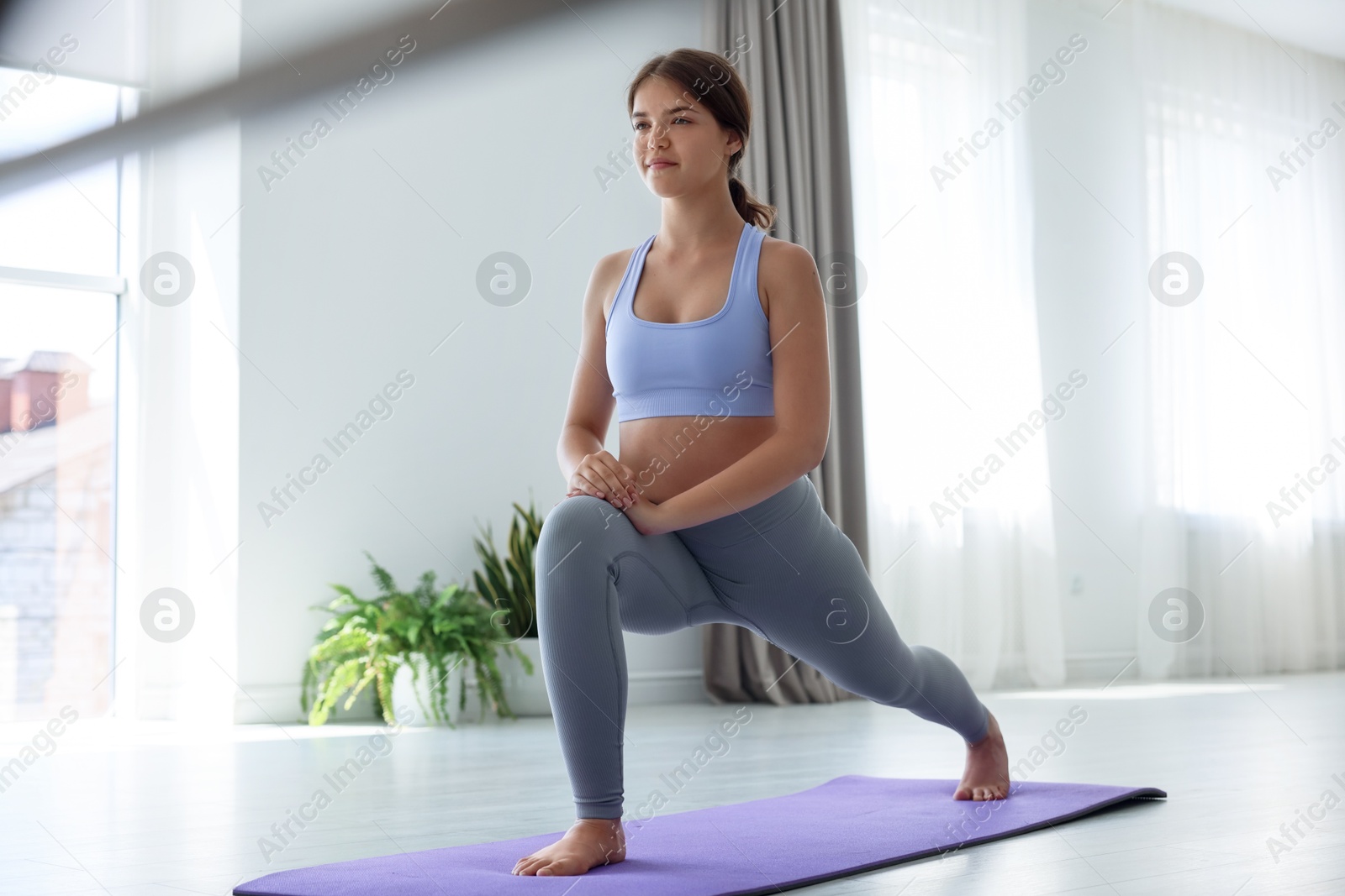 Photo of Teenage girl in sportswear stretching on mat indoors