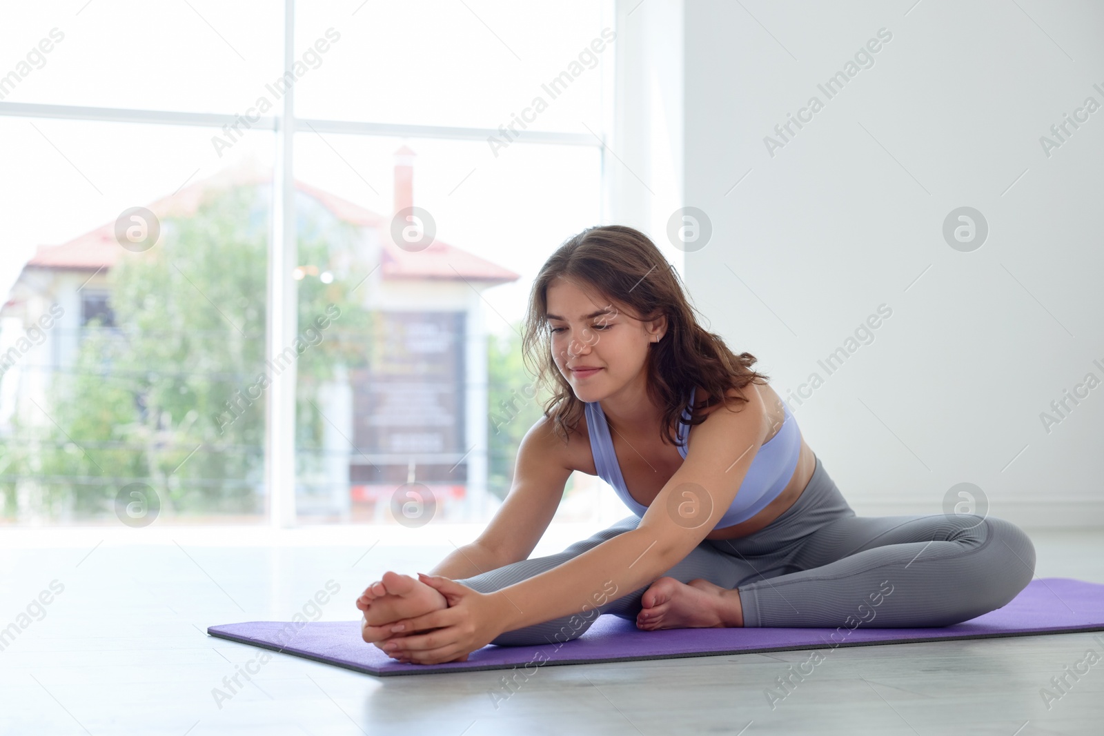 Teenage girl in sportswear stretching on mat indoors, space for text Photo of Teenage girl in sportswear stretching on mat indoors, space for text