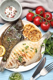 Photo of Tasty roasted flounder fish with herbs and lemon slices served on light blue wooden table, flat lay. Homemade seafood dish