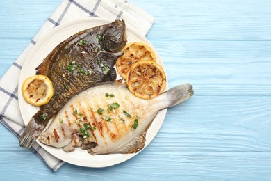 Photo of Homemade seafood dish. Tasty roasted flounder fish with herbs and lemon slices on light blue wooden table, top view. Space for text