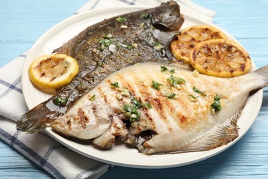 Photo of Tasty roasted flounder fish with herbs and lemon slices on light blue wooden table, closeup. Homemade seafood dish
